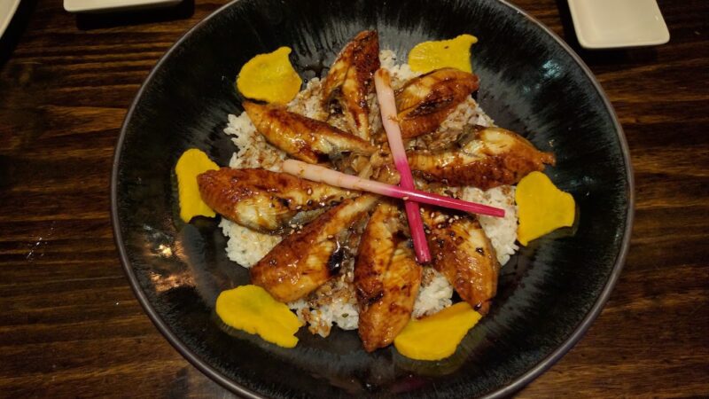 Grilled chicken with mango slices and garnish on a black plate.