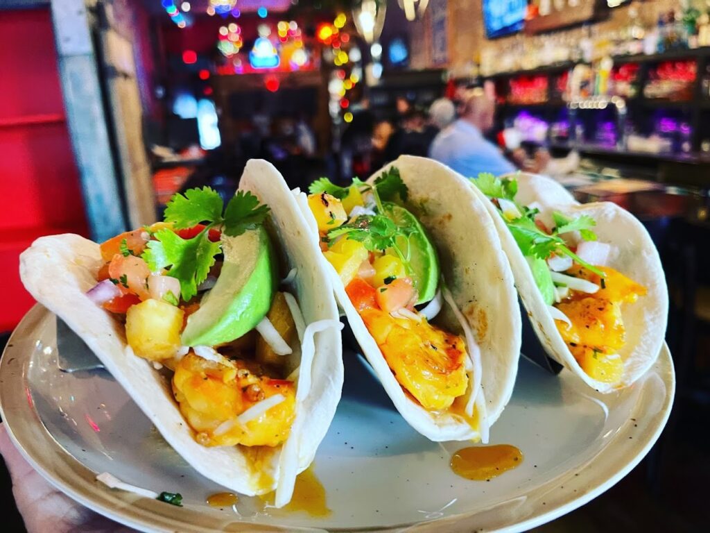 Three shrimp tacos on a plate at a bar.