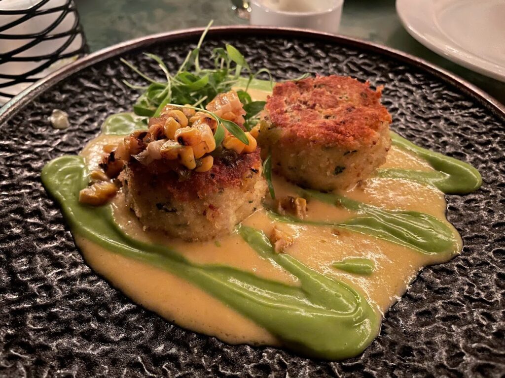 Two crab cakes on a plate with green sauce.